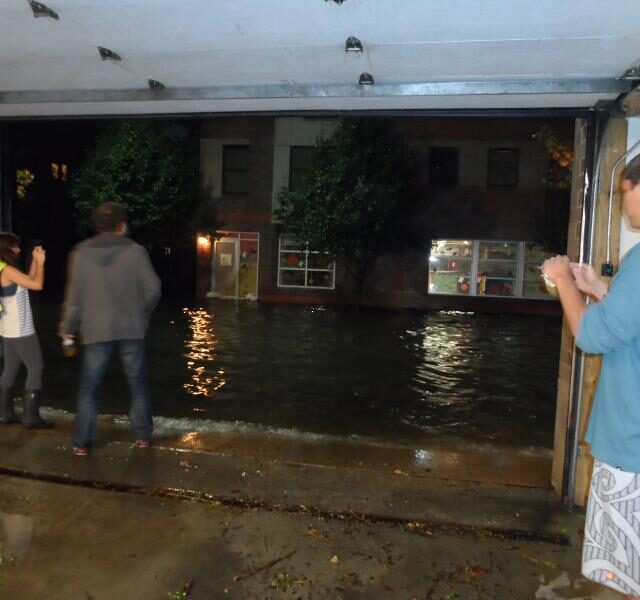 wave of water in city street with people standing in open garage door