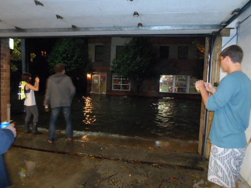 wave of water in city street with people standing in open garage door