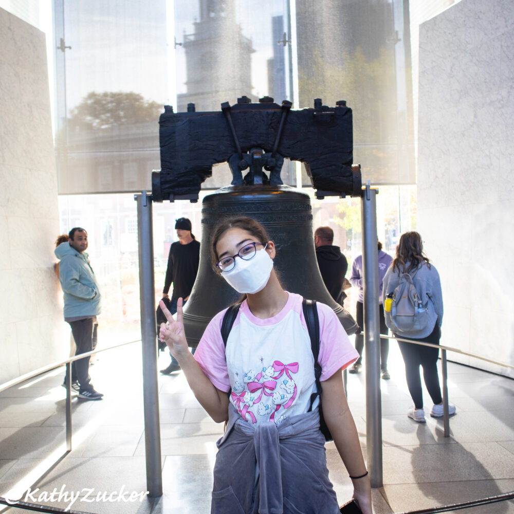 Young girl wearing medical mask standing in front of Liberty Bell