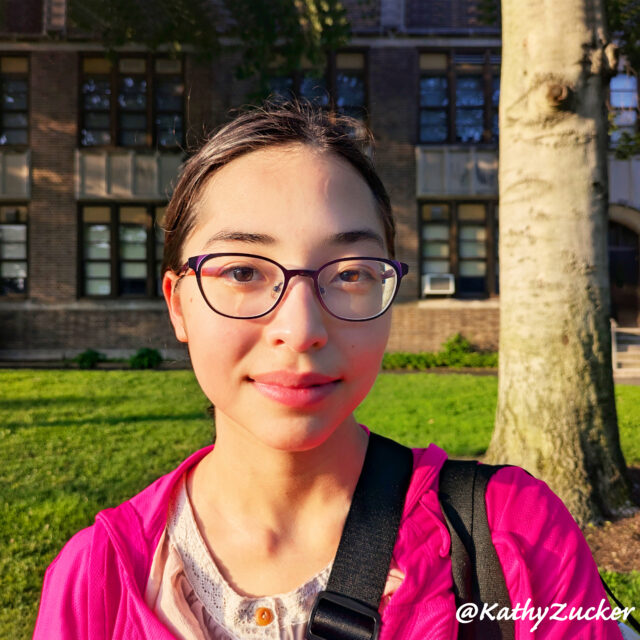 A young girl stands on the lawn of a suburban high school